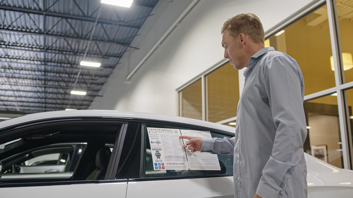 man pointing at leasing information sheet on car window